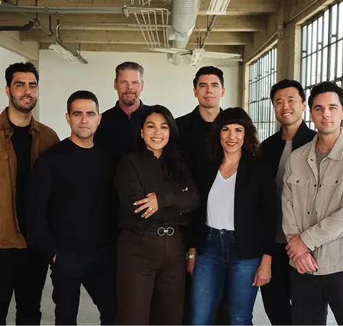 Group of seven diverse professionals smiling and standing inside a spacious industrial-style office.