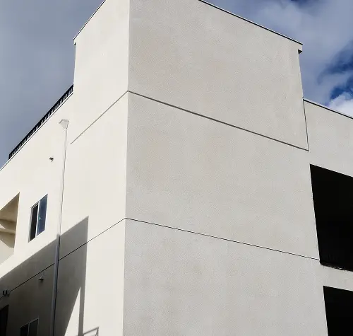 Modern white building corner with clean textured walls under partly cloudy sky.